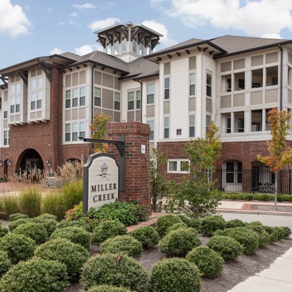 Distinctive sign of Miller Creek at Germantown, nestled amidst vibrant bushes and plants in front of the apartment buildings.